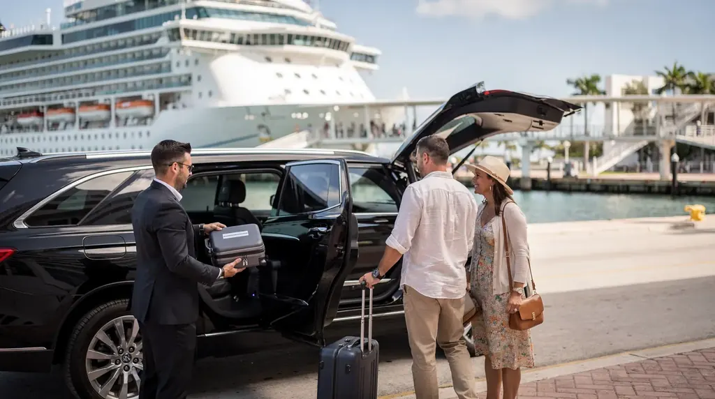 Chauffeur loading a couple’s luggage into a black SUV with a cruise ship docked behind them