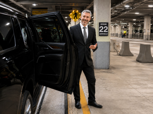 Chauffeur opening the rear door of a black SUV at the Miami airport arrivals curb